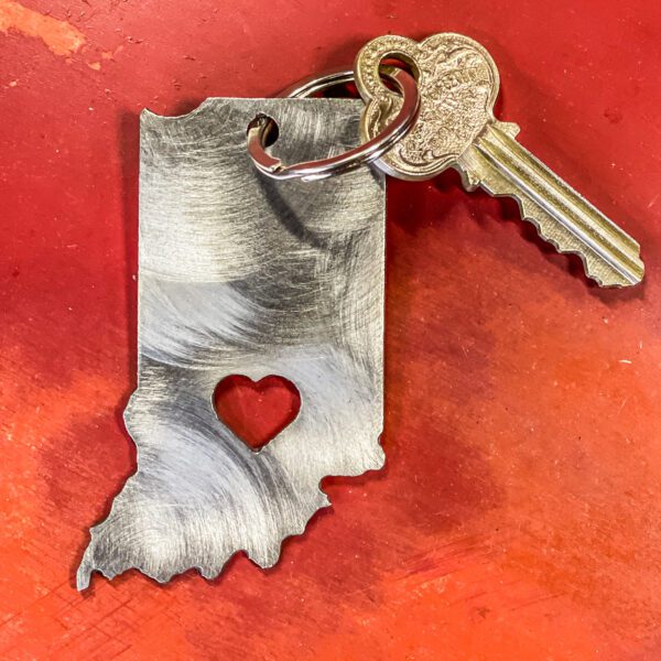 A key attached to a metal keychain shaped like indiana with a heart cutout, placed on a red surface.