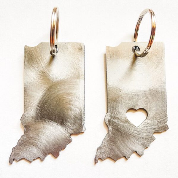 Two brushed metal keychains with irregular, ragged edges; one has a heart-shaped cutout.