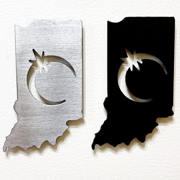 Two Indiana Solar Eclipse Magnets shaped like indiana state outlines, one silver and one black, each featuring a cut-out of a crescent moon and star symbol.