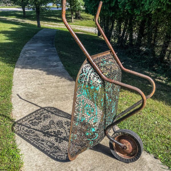 A metal wheelbarrow sitting on a sidewalk.