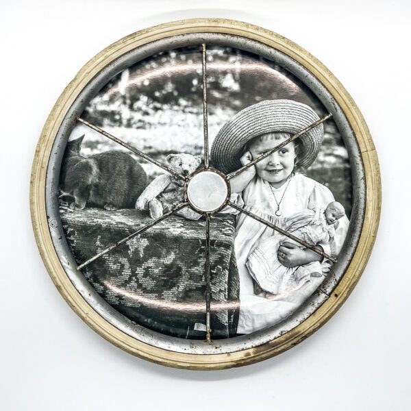 A vintage baby buggy wheel picture frame of a child in a hat on a wall.