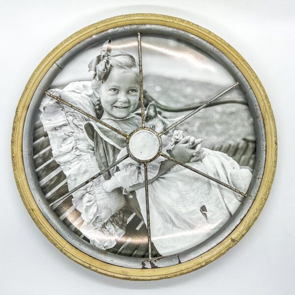 A photo of a little girl on a vintage baby buggy wheel picture frame.