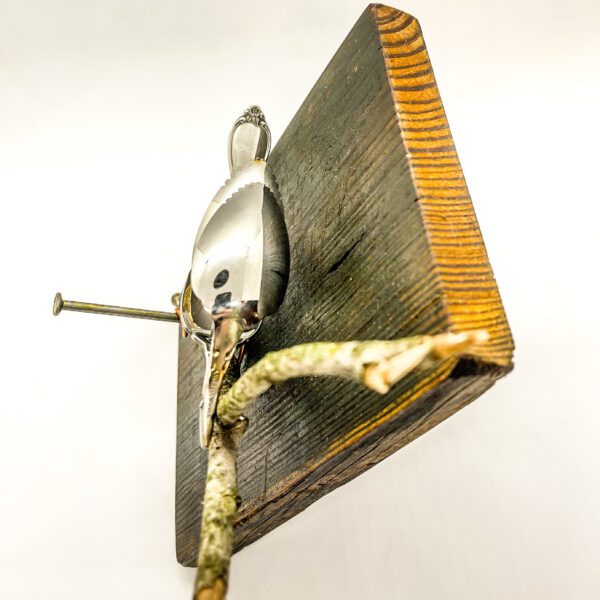 A Silverware bird is sitting on top of a piece of wood.