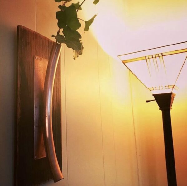 A Sconce Style Salvaged Copper Vase hanging on a wall next to a lamp.